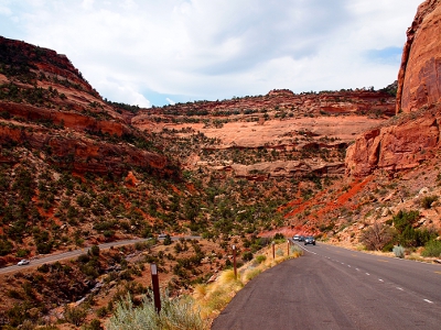 [Looking back at the u-shaped bend in the road winding through and up the canyon wall. In this image you are completely inside the canyon although cloudy blue skies can be seen at the top of the photo.]